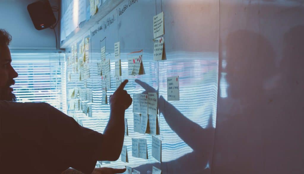 a person pointing at sticky notes on a glass wall